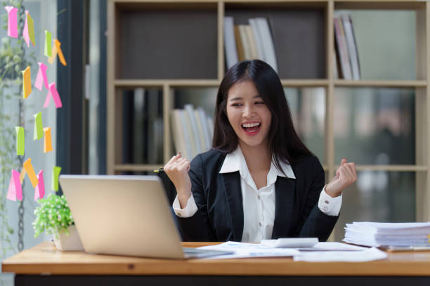 asian businessperson using laptop and celebrating victory and success, have good news, job celebrating achievement. - news of the world imagens e fotografias de stock