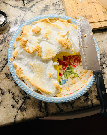 A freshly made lemon meringue pie with a fourth cut out of it in pretty dish