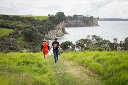 Couple holding hands, walking the Long Bay coastal walk. Auckland.