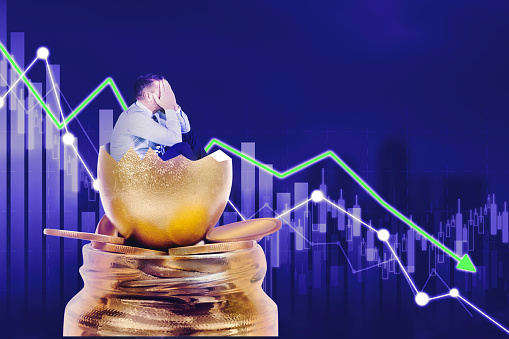 Frustrated businessman inside a cracked golden egg can not watch the market crash with chart background