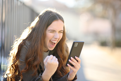 Excited woman checks phone news outdoors
