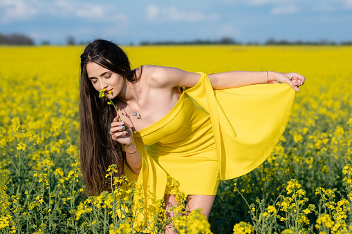 Beautiful young woman enjoying a sunny spring day in a yellow field of wildflowers