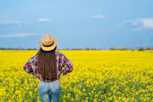 Young female farmer with a straw hat standing in the rapeseed field