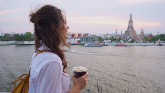 Woman drinking coffee and looking at Wat Arun and Chao Phraya river