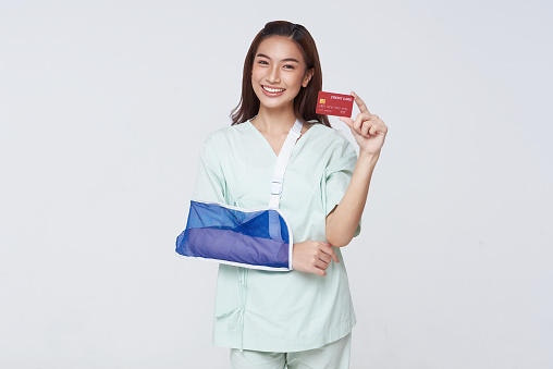 Happy smile asian woman patient put on a cast showing credit card isolated on white background. Healthcare services expenses, money savings on health insurance, medicine cost concept.
