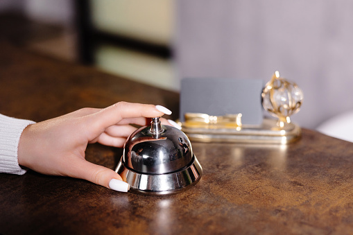 Hand of guest ringing bell on reception desk of in hotel