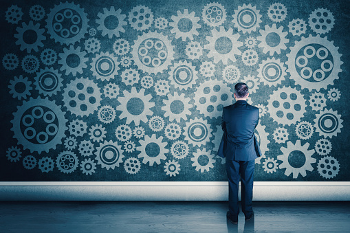 Back view of businessman looking at cogwheels drawing on wall