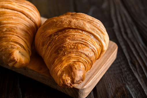 Two croissants on a wooden cutting board. Rustic dark table. Food banner. Tasty fresh croissant, jam, orange juice. Continental breakfast served with freshly baked pastry. Close up view, Good morning.  space for text, mockup. mock up for advertising, ad