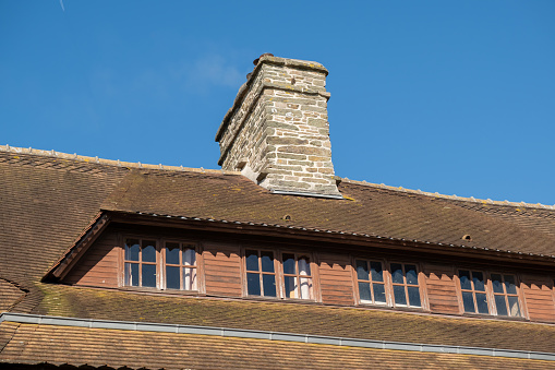 Stone chimney and part of roof made of tiles of old house against blue clear sky