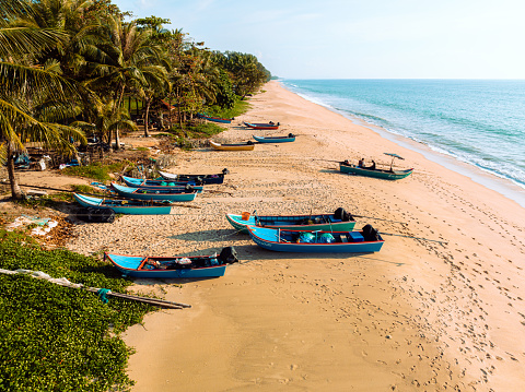 Stranded Thai Long Tail Fishing Boats at the Beach of Mueang National Park under blue summer sky. Mid Air Drone Point of View towards the boats and beach. Mueang National Park Beach,  Phang Nga District, North of Phuket, Thailand, Southeast Asia.