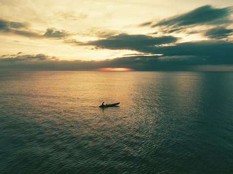 Thailand Fisherman sitting a small typical thai fishing longtail boat fishing during sunset in the Andaman Sea under moody orange dusk skyscape. Drone Point of View. Moody sunset over the Andaman Sea, Thailand, Southeast Asia.