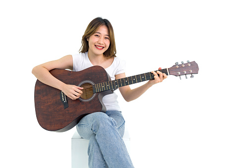 Young asian woman in white t-shirt and jean playing acoustic guitar. Portrait on white background with studio light.