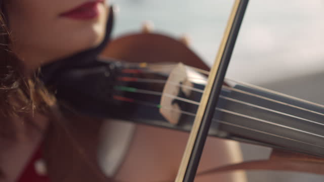 Close-up violin bow in female hands playing strings of musical instrument outdoors. Unrecognizable Caucasian talented lady enjoying music in sunshine.