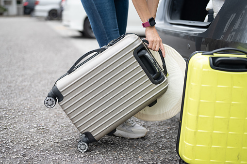 Shot of a woman is try pulling heavy luggage into the car boot.