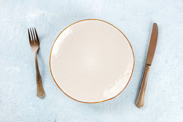 istock An empty white plate with a gold rim, with a fork and a knife, overhead 1481143455