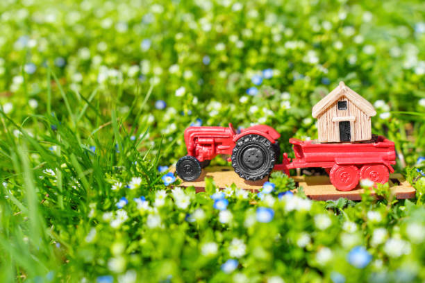 istock Toy Tractor Transporting a Tiny House on a Flower Meadow 1481144426