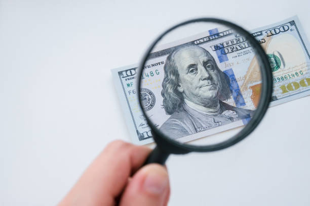 istock Magnifying glass and dollar currency on a white background. 100 dollars banknote view through a magnifying glass. Hand holding the lens. High quality photo. 1481144684