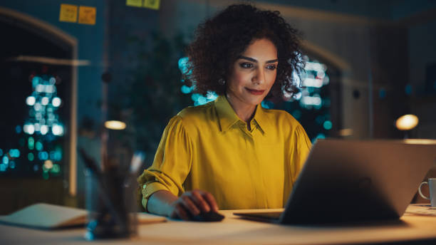 istock Beautiful Middle Eastern Manager Sitting at a Desk in Creative Office in the Evening. Young Stylish Female Using Laptop Computer in Marketing Agency, Developing Projects and Schedules 1481144711