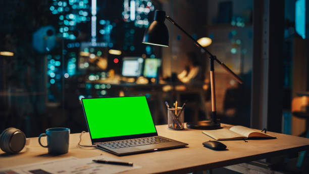 istock Laptop Computer with a Green Screen Chromakey Mock Up Display Standing on a Desk in the Office at Night. Modern Open Space Creative Agency with Manager Working in the Background. 1481145909