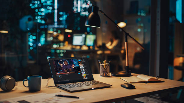 Laptop Standing on a Desk with a Video Streaming Platform Displayed on Screen. Table with Computer, Coffee Mug, Headphones and Notebook in Creative Office at Night.