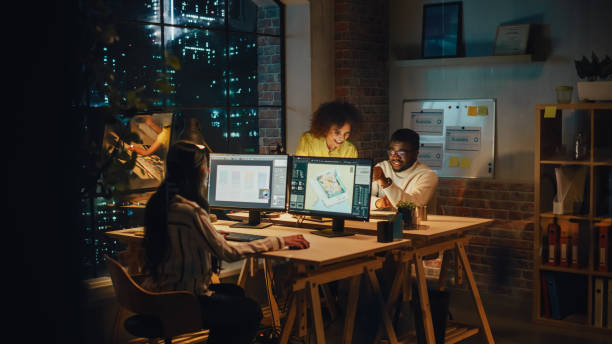 istock Small Diverse Multiethnic Group Collaborate on a Project and Work Together in an Office at Night. Team Leader Talking with a Professional, Laughing, Discussing Changes to a Software Design. 1481146412