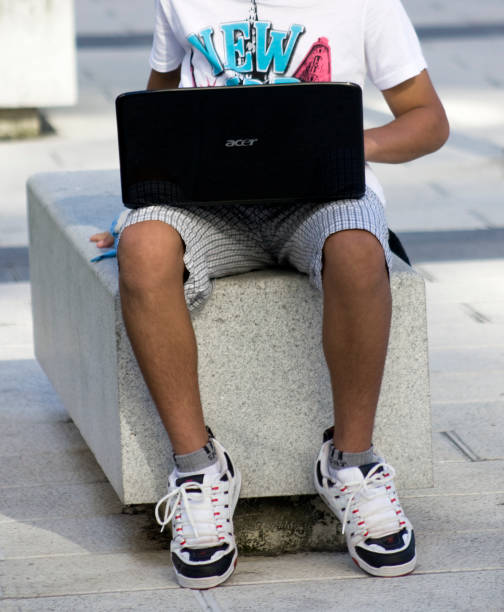 Young man using laptop in the street.   student sitting on stone bench working with laptop, preparing for exams outdoors, having rest in university campus. Technology, education and remote working concept, copy space