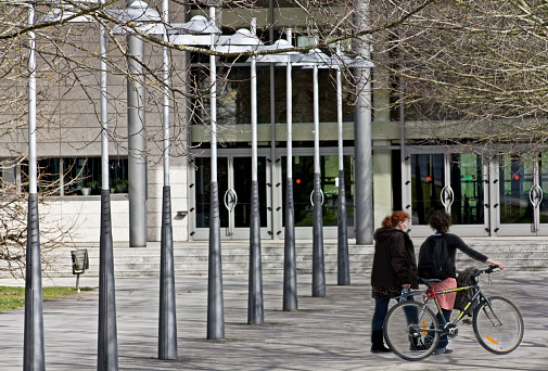 Lugo , Spain- February 23, 2011: Rear view of young women walking and talking in Lugo city campus town square, Santiago de Compostela University, one of them pushing a bicycle..