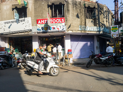 Nagpur, Maharashtra, India - March 2019: A man riding a motorbike past the rustic facade of an old building in a busy market street in the city.