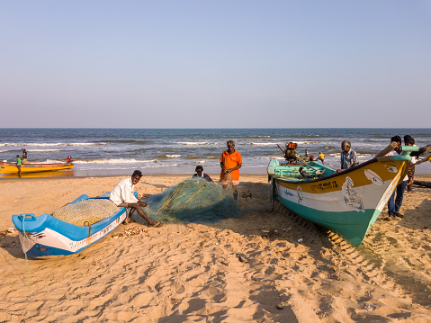 Chennai, India - February 2020: Fishermen working with fishing nets beside their wooden boats on Elliot's beach in Besant Nagar.