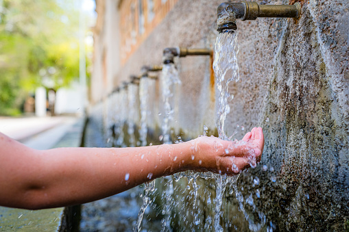 Close up of a hand playing with water flowing from fountain in an old town of Spain. High resolution 42Mp outdoors digital capture taken with SONY A7rII and Zeiss Batis 40mm F2.0 CF lens