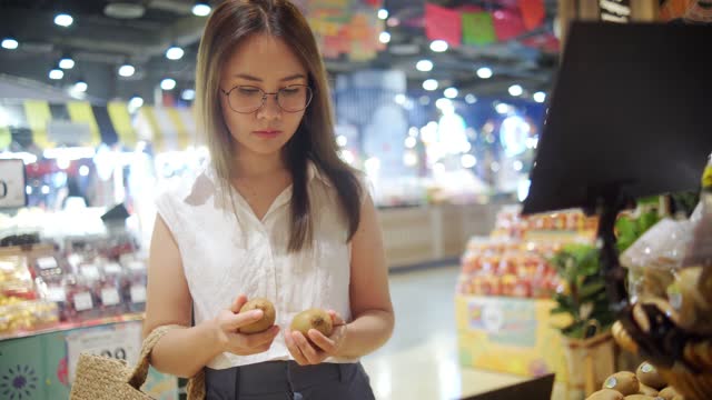 Young asian woman shopping for kiwifruit, fruits and vegetables, in supermarket grocery, Vegan food lifestyle concept.