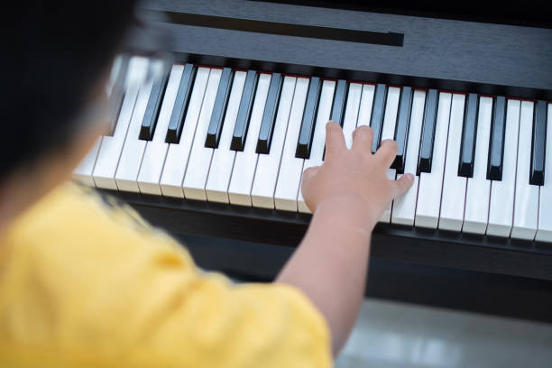 garotinho asiático tocando piano clássico na sala de estar em casa. vista traseira. - child prodigy - fotografias e filmes do acervo