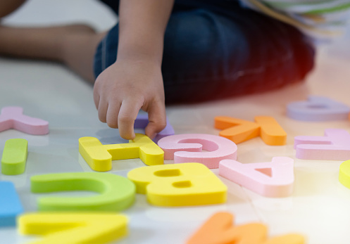 Selective focus. Toddler boy learning alphabet letter on the floor at home. Intellectual game preschool primary education concept.