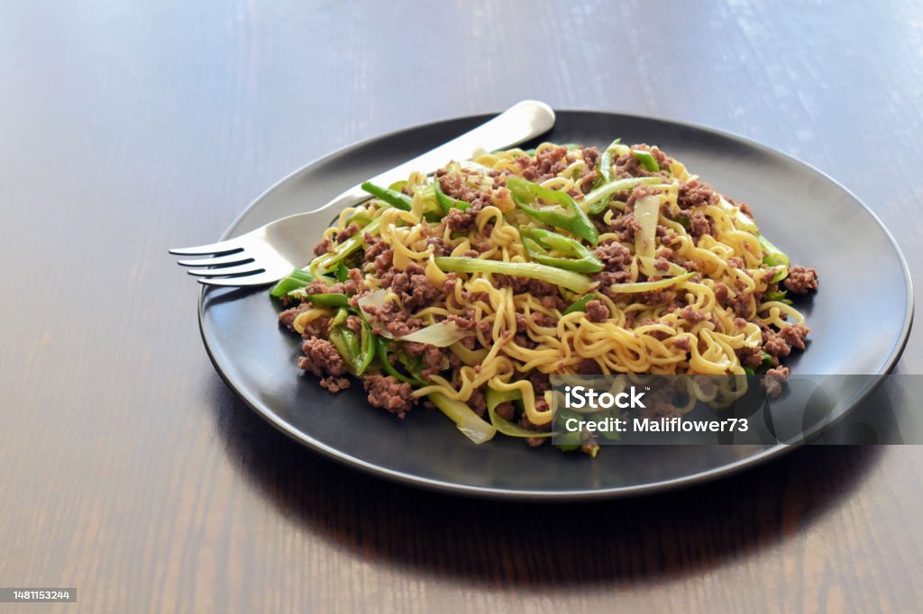 Stir fry noodles with minced beef, spring onion and chillies on a black plate. Stir fry noodles with minced beef, spring onion and chillies on a black plate. Spicy noodles on the table. Asian Food Stock Photo