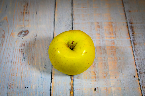 A whole yellow, golden apple on an old, off-white wooden plank table.