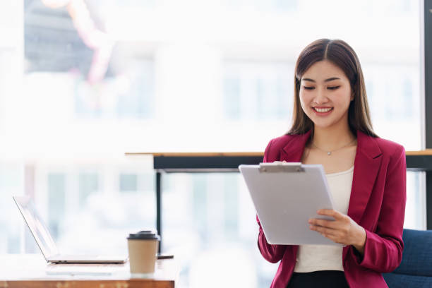 istock Smiling Asian Banker makes financial report and studies annual figures, analyzes profits. Accountant checks status of financial 1481156573