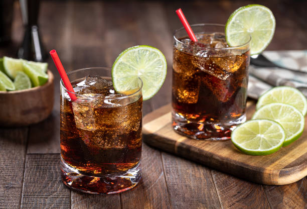 Rum and cola cocktail with lime slice Rum and cola cocktail with lime slice on rustic wooden table cuba libre stock pictures, royalty-free photos & images