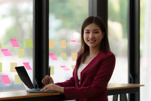 istock Smiling Asian Banker makes financial report and studies annual figures, analyzes profits. Accountant checks status of financial 1481158254