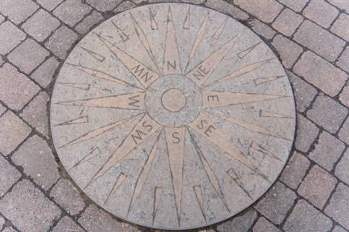 Amble, United Kingdom – March 11, 2023: A stone plaque of the compass points on the pavement in the town square of Amble, Northumberland, UK.