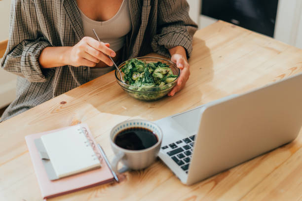 istock A woman eats a salad while sitting at a table while working on a laptop. 1481165087