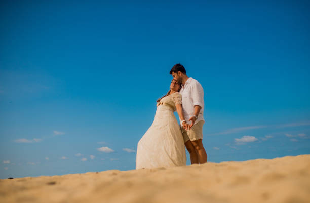 married couple outdoors on the beach embracing each other in a white dress