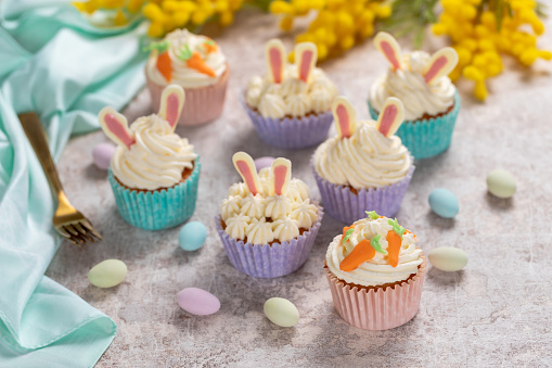 Easter cupcake with cream cheese frosting decorated with carrots and bunny ears.