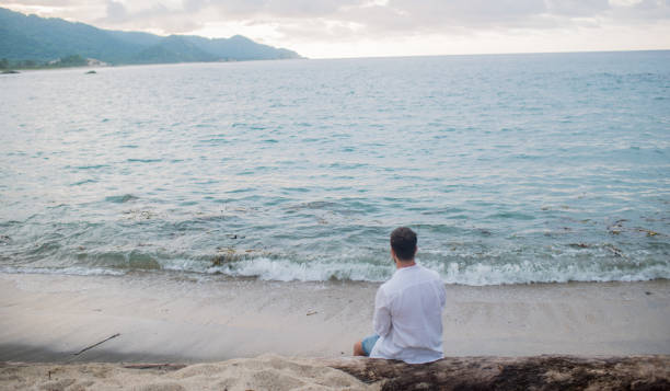 istock Single man sitting alone looking at the horizon at sunset during sunset on vacation 1481171993