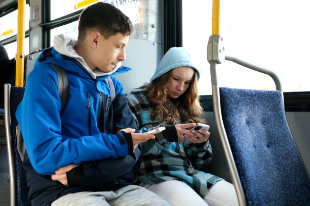 interior of crowded bus with passengers listening to music and using mobile phone. two teenagers in blue clothes sit on a bus canada vancouver hoods autumn winter spring tracksuits use a mobile phone - bus transportation indoors people imagens e fotografias de stock