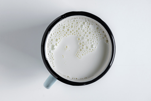 White milk in a metal mug on a white background, close up, top view. Dairy product concept