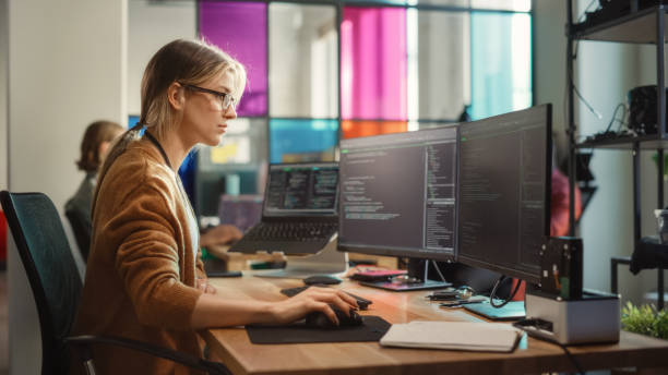 Caucasian Woman Coding on Desktop PC and Laptop Setup With Multiple Displays in Spacious Office. Female Junior Software Engineer Working on New Sprint of Mobile Application Development For Start-up. mujer caucásica codificación en pc de escritorio y configuración de computadora portátil con múltiples pantallas en una oficina espaciosa. ingeniera de software junior que trabaja en un nuevo sprint de desarrollo de aplicaciones móviles para la puest