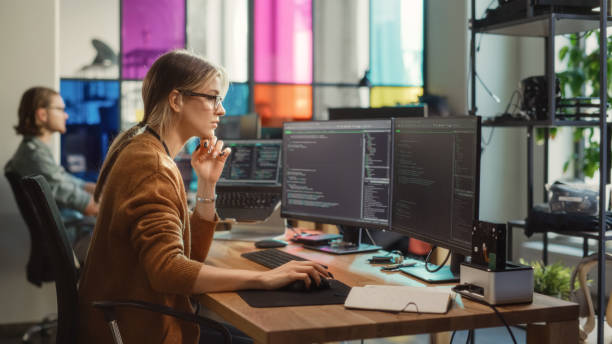 donna caucasica scrive righe di codice su pc desktop con più display e un laptop in un ufficio elegante. scienziata di dati femminile professionista che utilizza il software per analizzare le informazioni da internet. - pc desktop pc women desk foto e immagini stock