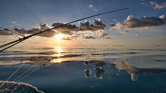 The outrigger and side of a fishing boat in calm seas with the sun setting off the coast of the Marquesas in Florida.