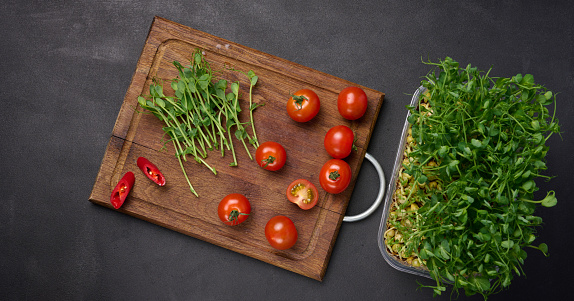 Red tomato and sprouted pea seeds on a black background, microgreens for salad, detox. Top view