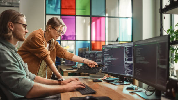 istock Female Senior Software Engineer Gives Advice to Male Junior Developer, Pointing at Desktop Computer Display With Code. Caucasian Woman Offers New Features, Helps Fixing Bugs in Modern SaaS Platform. 1481182787